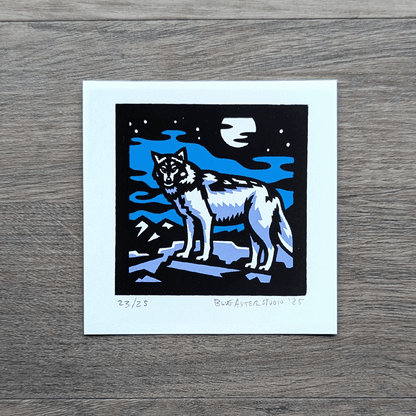 A square screen printed artwork of a gray wolf standing on a flat rock with mountains in the distance. A full moon shines above.