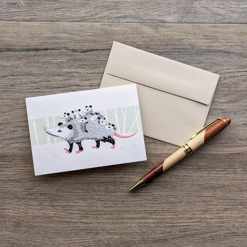 A notecard measuring 3.5 xby 5 inches, featuring an illustration of a mother opossum with several babies on her back, with a green forest background. Notecard lies on a beige natural color envelope.