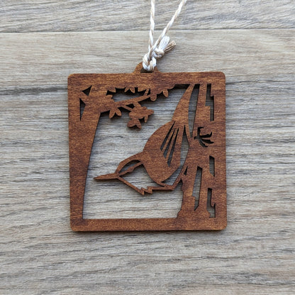 A wooden laser cut ornament of a nuthatch perched on a tree colored with brown wood dye on a gray wood background.