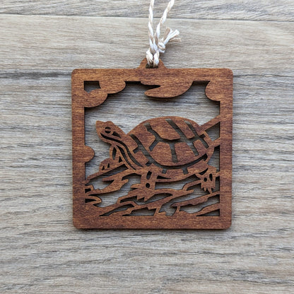 A wooden laser cut ornament of a turtle sitting on a log colored with brown wood dye on a gray wood background.