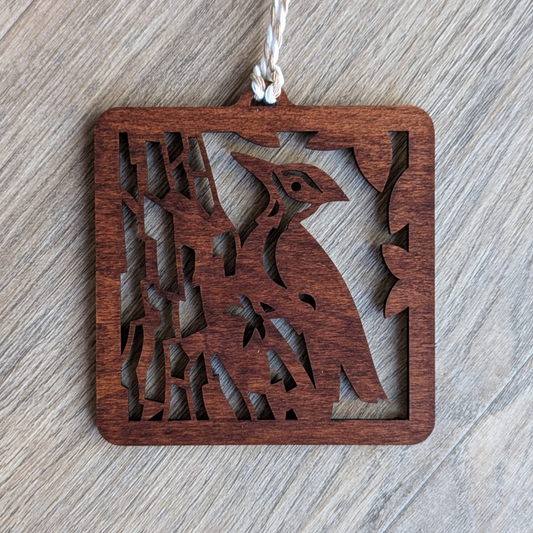 A brown wooden laser cut ornament of a pileated woodpecker climbing a tree trunk.