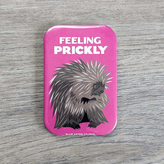 A rounded rectangle magnet of a grumpy porcupine with arms crossed under the text Feeling Prickly.