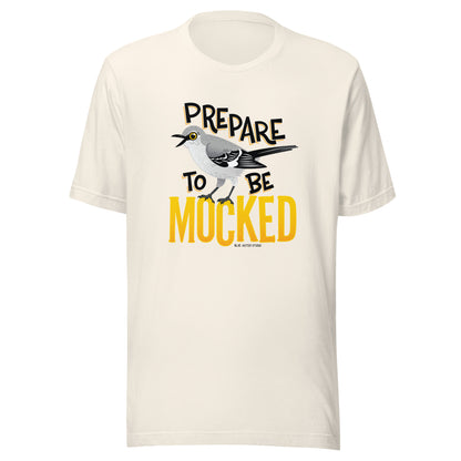 A creme tee shirt with the text "prepare to be mocked" with an illustrated mockingbird perched within it