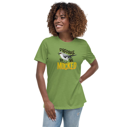 A green women's cut tee shirt worn by a dark skinned female model, with the text "prepare to be mocked" with an illustrated mockingbird perched within it