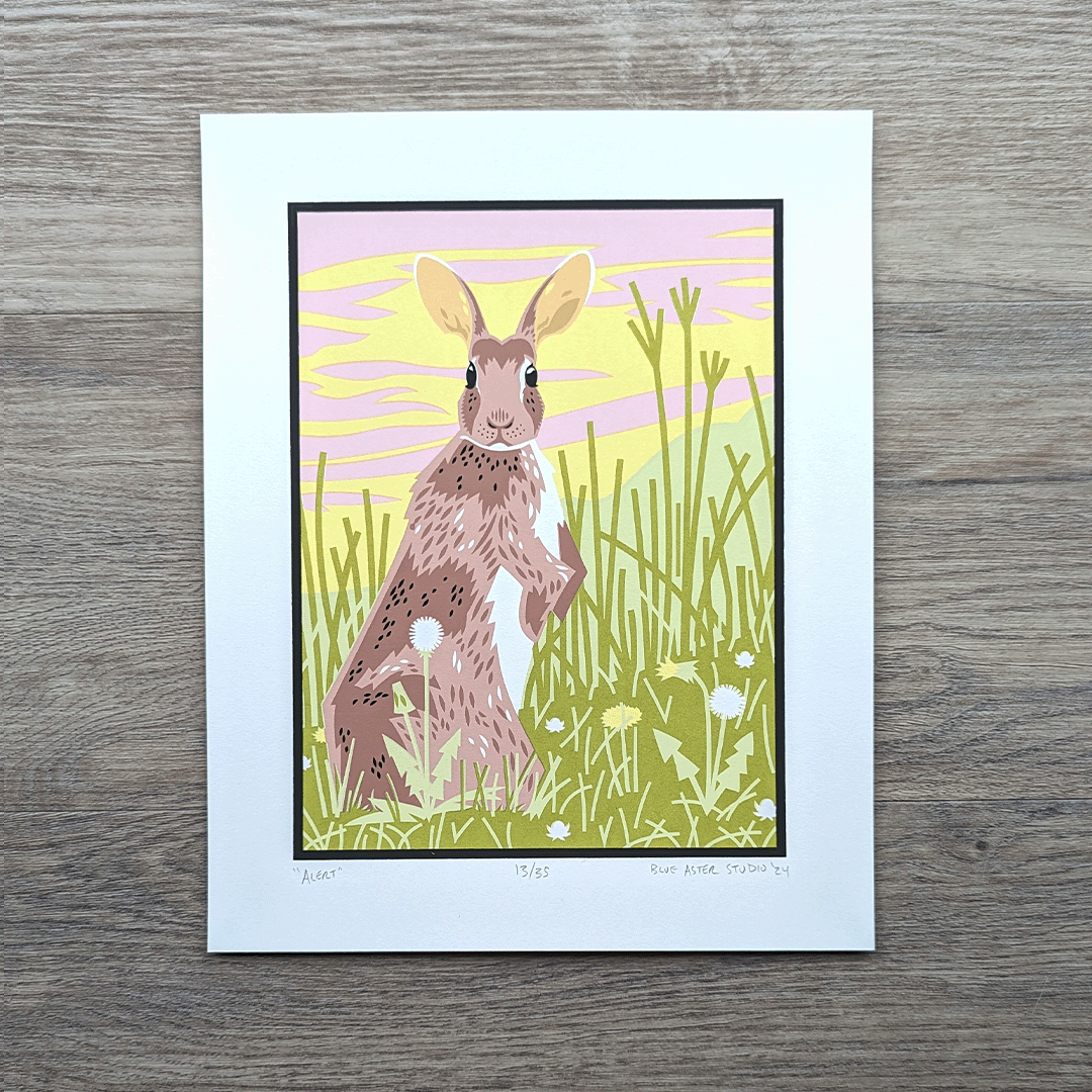 An 8 inch by 10 inch screen printed illustration of a cottontail rabbit standing alert in a tall grass meadow in front of a pink and yellow sky.
