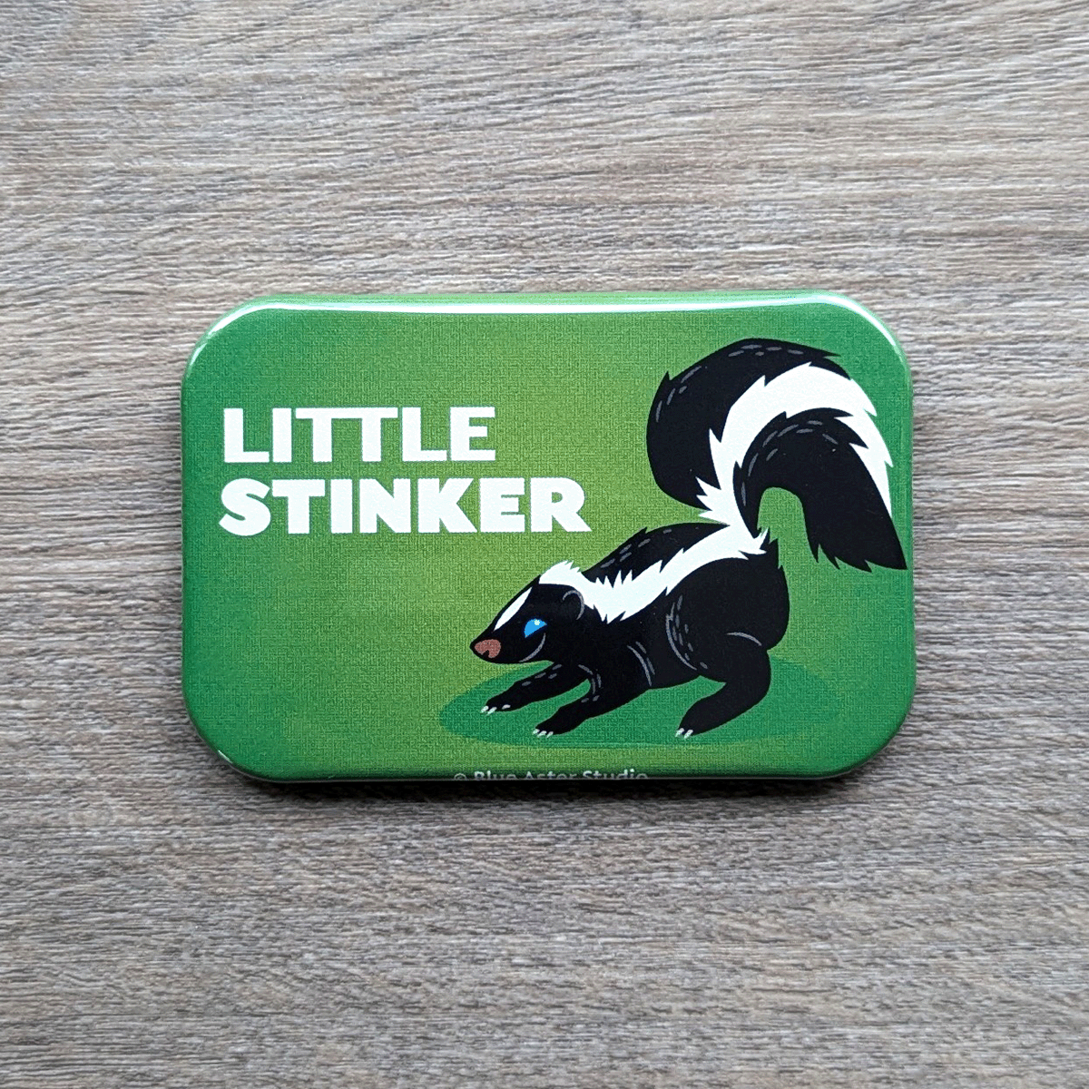 A 2 inch by 3 inch refrigerator magnet which features an illustration of a cute skunk and the words Little Stinker.