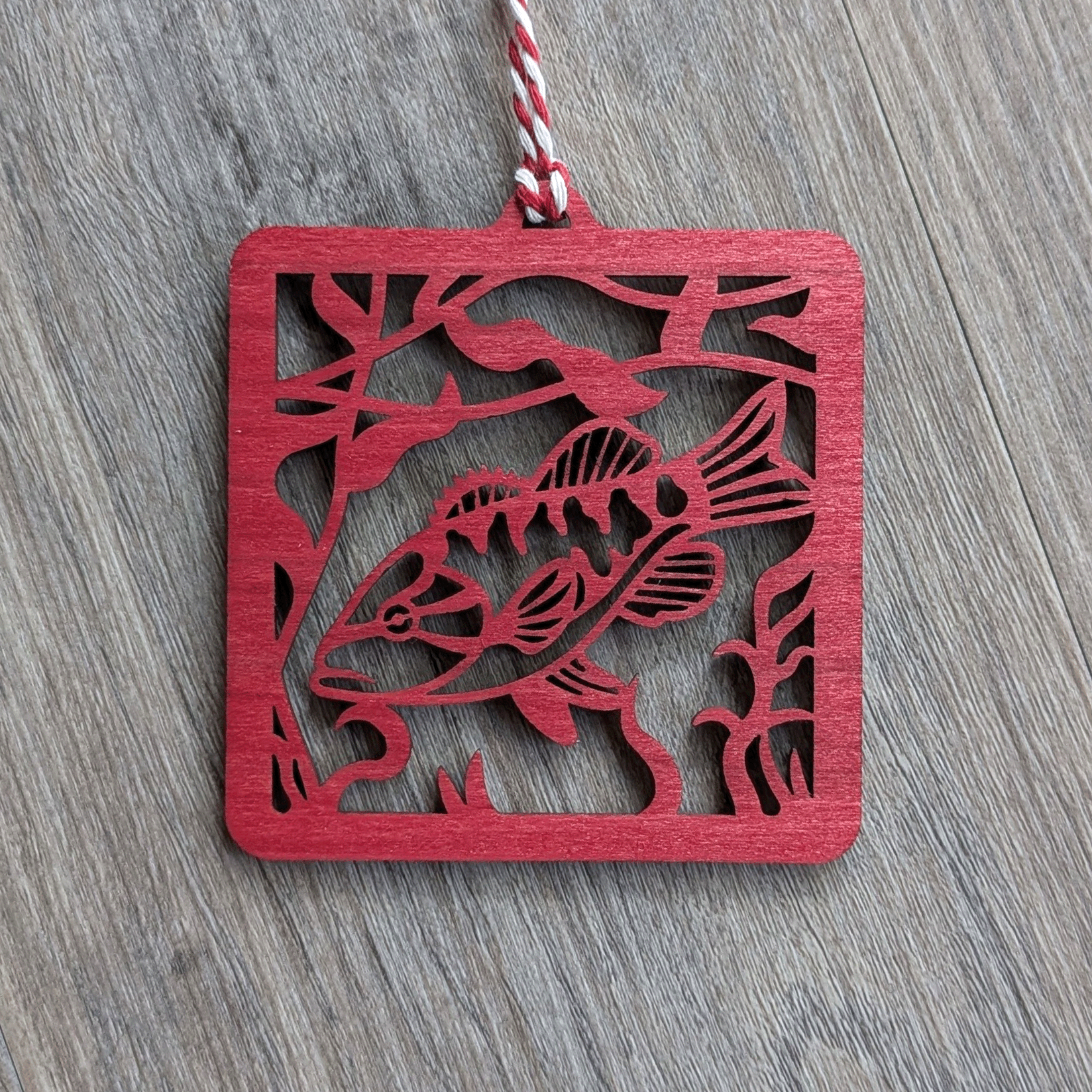 A square red wooden ornament of a smallmouth bass.