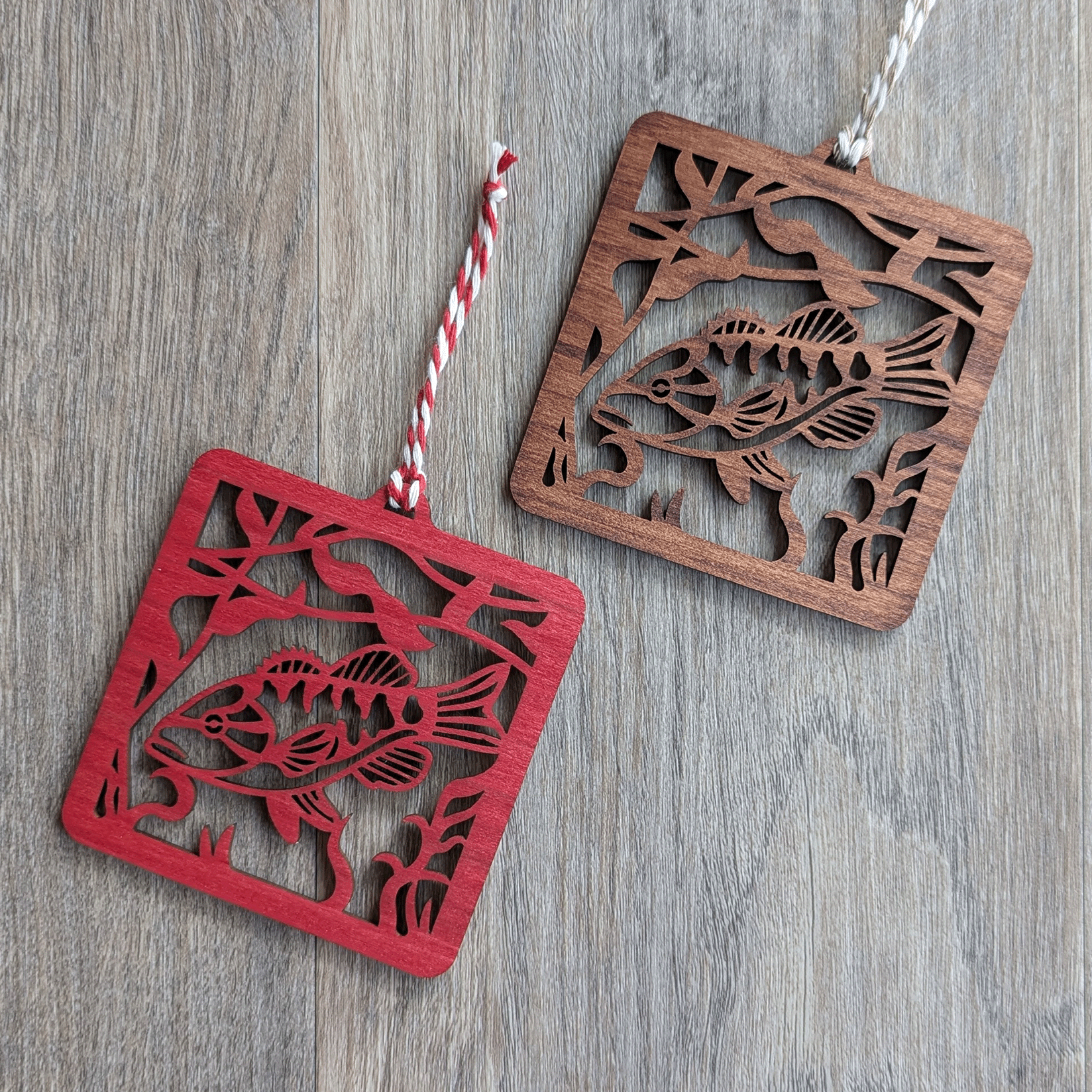 Two square wooden ornaments of a smallmouth bass, one stained red and the other brown.