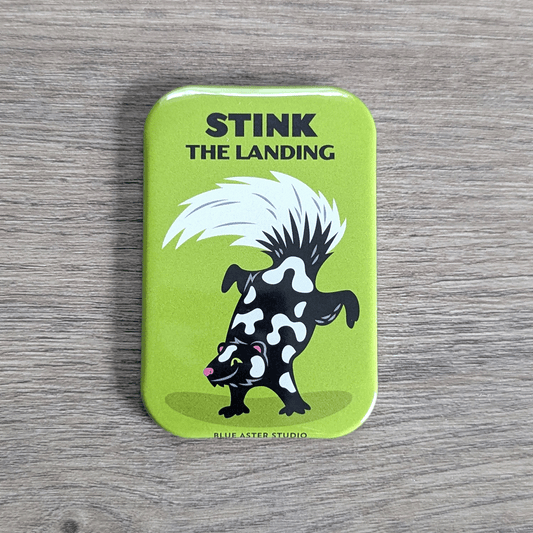 A rounded rectangle magnet featuring an illustration of a spotted skunk doing a hand stand under the text Stink the Landing.