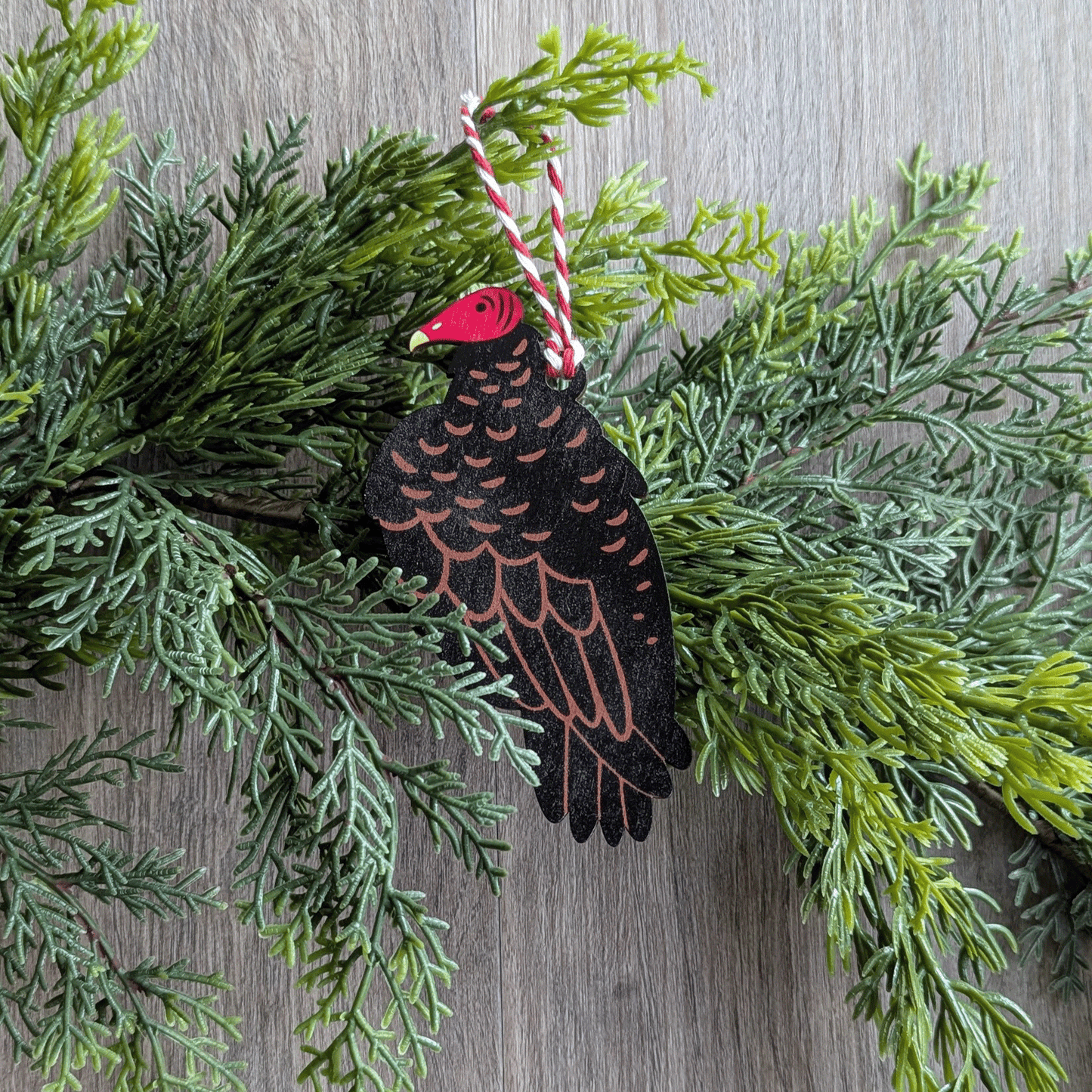 A wooden screen printed ornament of a turkey vulture hanging on a hemlock garland.