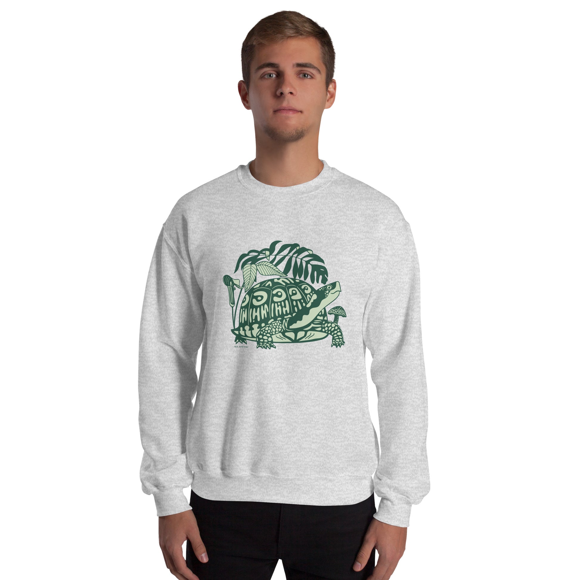 A man wearing a light gray crew neck sweatshirt with a design of a box turtle surrounded by woodland plants.