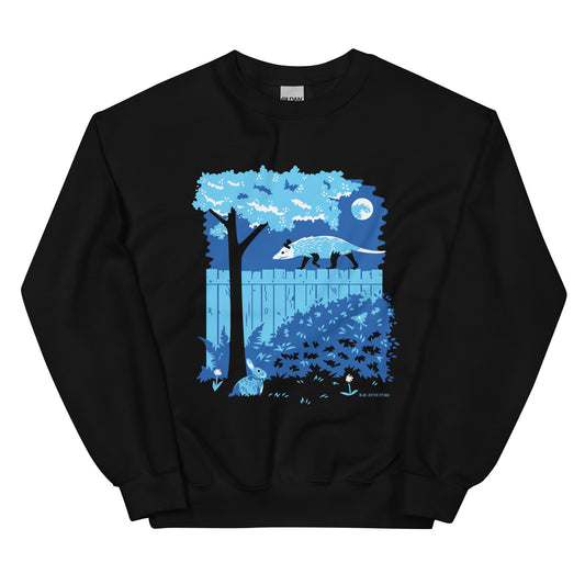A black sweatshirt with an illustration of an opossum walking on a moonlit fence with a rabbit and a luna moth in the yard below.