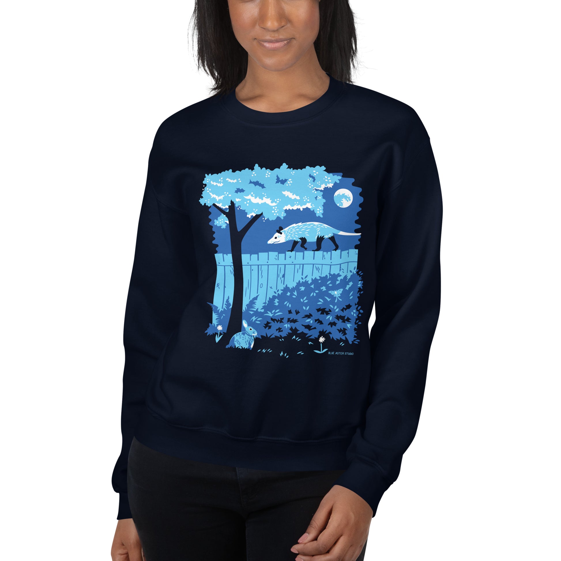 A model wearing the navy blue illustrated opossum and bunny night time backyard sweatshirt.