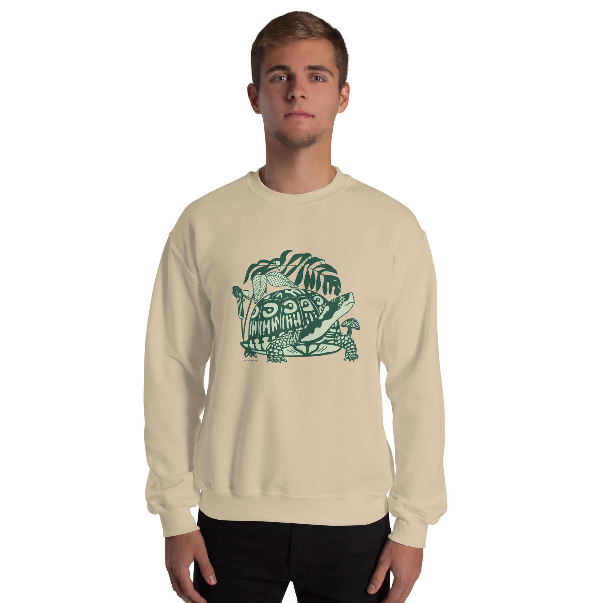 A man wearing a light beige crew neck sweatshirt with a design of a box turtle surrounded by woodland plants.