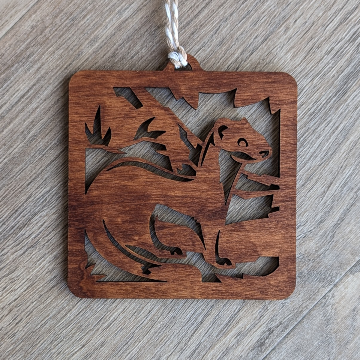 A brown wooden laser cut long-tailed weasel ornament.