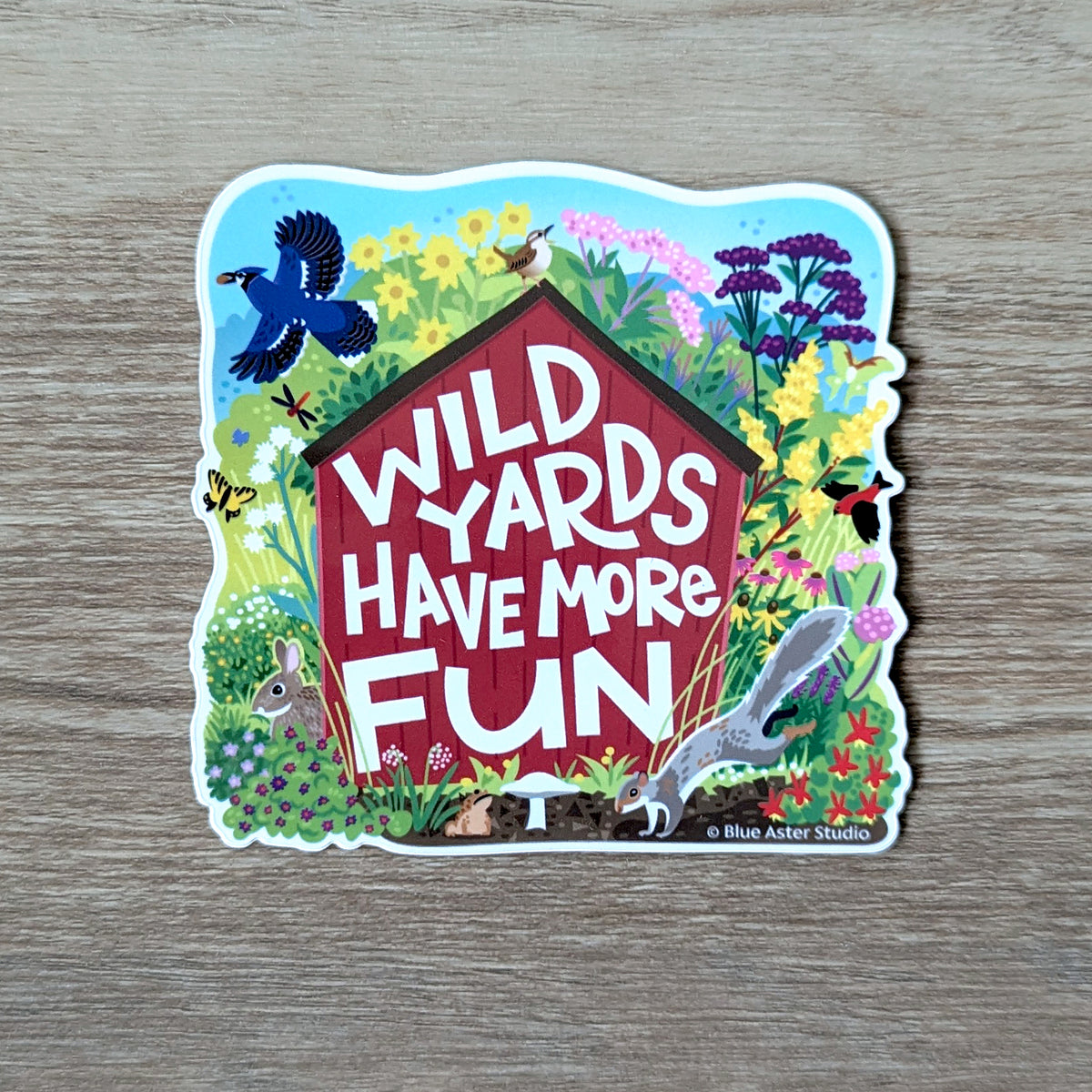 A sticker with a red shed surrounded by native plants and animals. The text on the shed reads "Wild Yards Have More Fun."