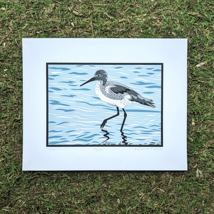 An original screen print of an illustration of a willet shorebird wading and foraging in shallow water. The print is sitting on a mossy background.