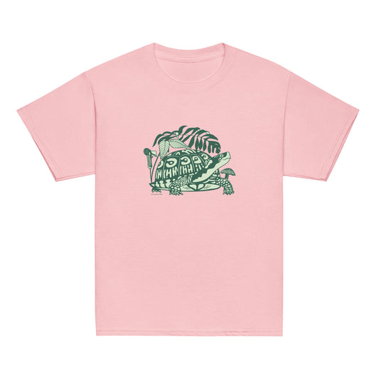 A pink youth-sized t-shirt with a design of a happy box turtle surrounded by native North American woodland plants.