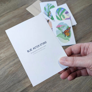A photo showing the back of the monarch butterfly cards. It has the Blue Aster Studio logo and website as well as a note that they are printed on recycled paper.