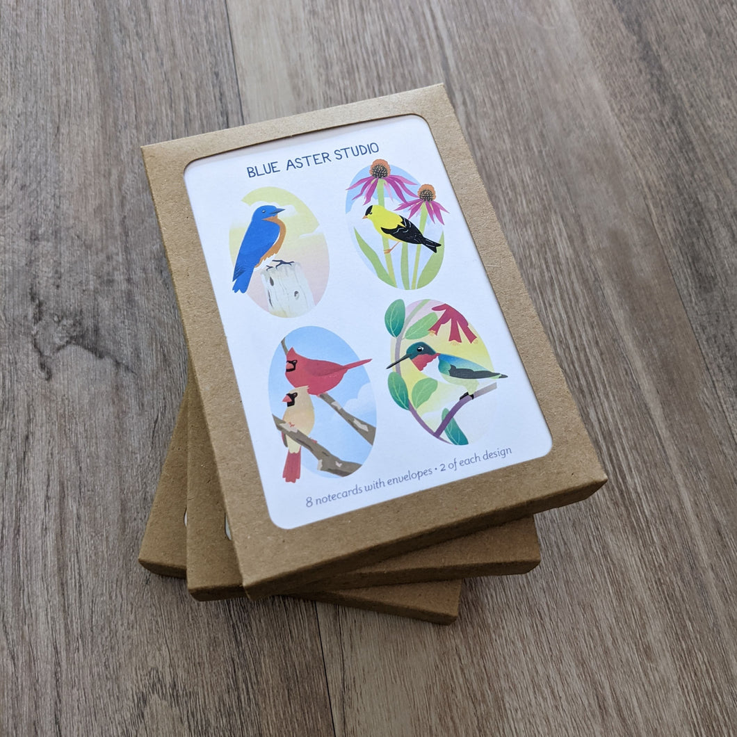 A package of notecards with a cover slip featuring the four illustrations featured on the cards. The birds are an eastern bluebird, an American goldfinch, a male and female American cardinal, and a ruby-throated hummingbird.
