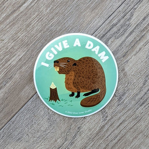 A beaver sticker featuring an illustration of a beaver next to a chewed on tree stump with the words "I Give A Dam" above it.