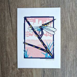 An illustrated art print of a dragonfly perched on a twig in an urban wetland setting. A frog peeks out of the water.