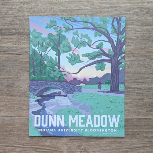 An art print of the view of Dunn Meadow on the Indiana University Bloomington campus. This illustration is of the view facing toward Indiana Street and shows off the Campus River and the bridge coming from the Indiana Memorial Union with a sunset in the background.