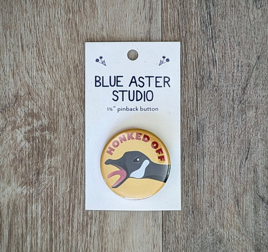 A 1.5 inch pinback button featuring an illustration of a goose with its beak open wide and the words "Honked Off" above it.