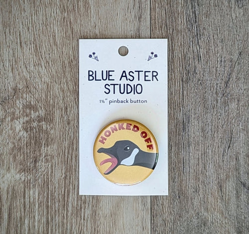 A 1.5 inch pinback button featuring an illustration of a goose with its beak open wide and the words 