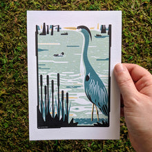Load image into Gallery viewer, A hand holding an art print of a heron in a swampy wetland.