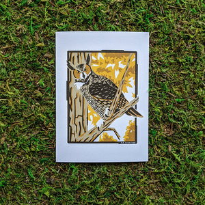 An art print of an illustration of a great horned owl perched in a tree surrounded by fall folliage.