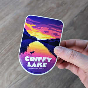 A Griffy Lake sticker that features a sunset being held to show scale.