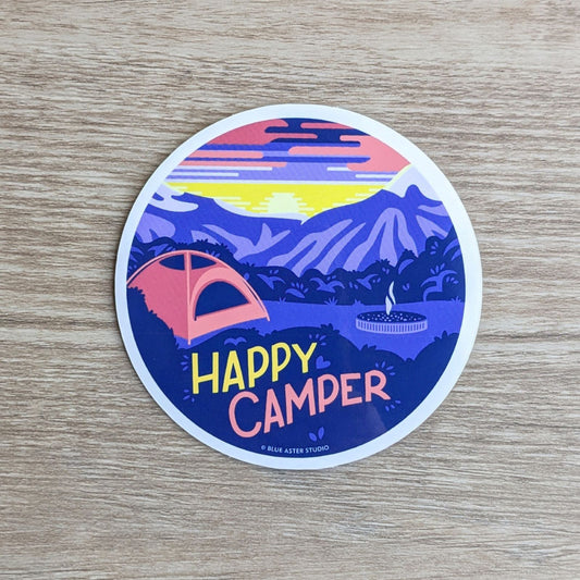 A round vinyl sticker depicting a campsite in the mountains at sunrise with the text "Happy Camper"