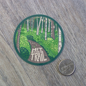 A Hit The Trail vinyl sticker next to a USD quarter for scale.