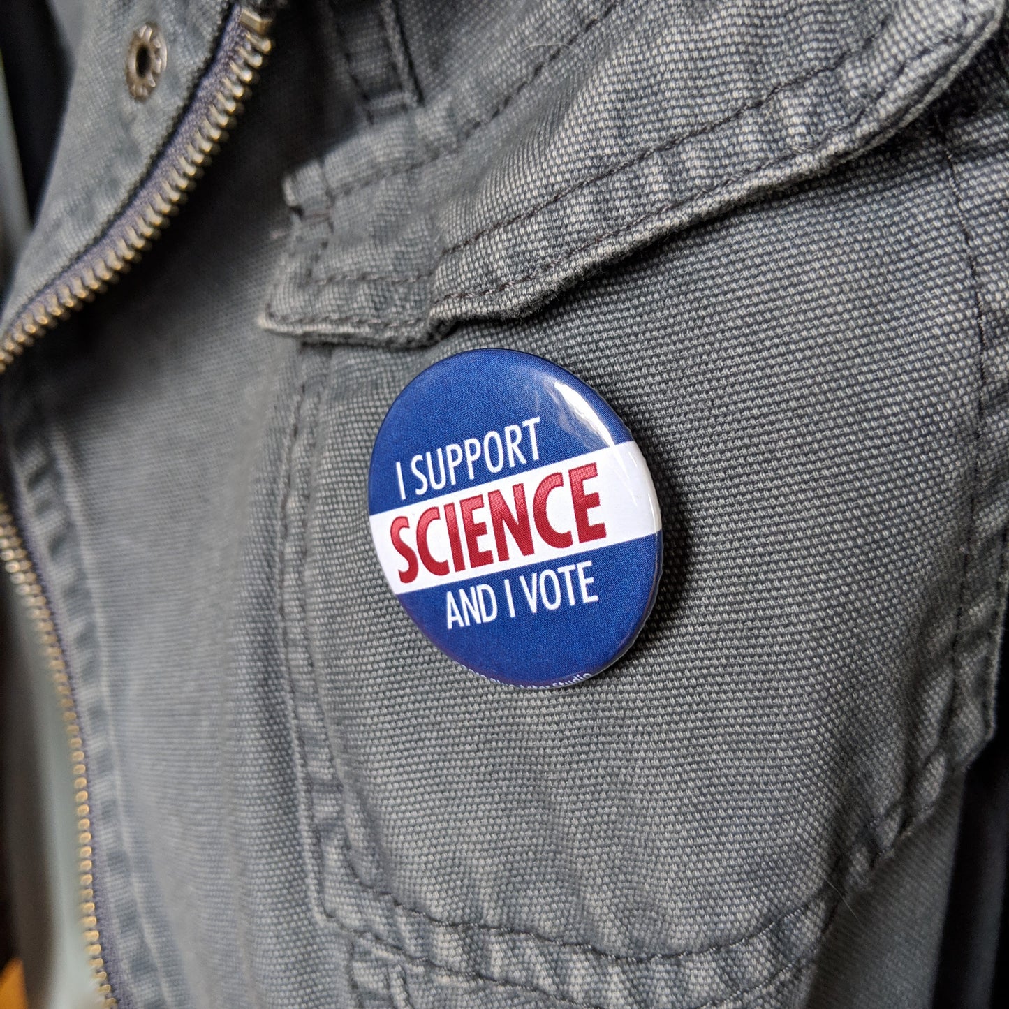 The I Support Science And I Vote button pinned to a gray canvas jacket.