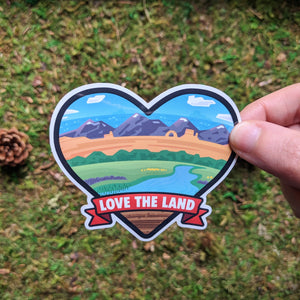 Hand holding the Love The Land vinyl sticker.