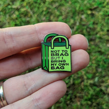Load image into Gallery viewer, The reusable bag enamel pin being held in a hand to show detail.