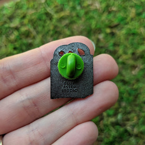 A hand holding the reusable tote bag enamel pin to show the back. It has a green rubber clutch and is stamped with Blue Aster Studio.
