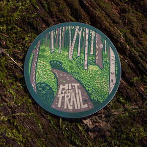 The hit the trail sticker out in the wild with a mossy background.