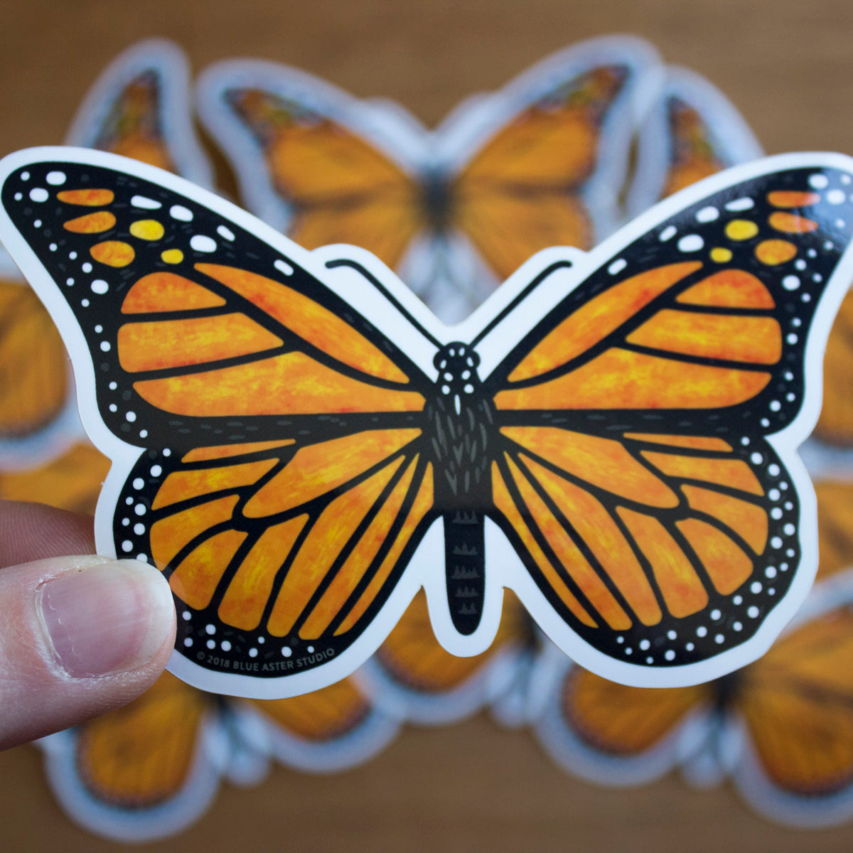 A hand holding a vinyl sticker of a monarch butterfly.
