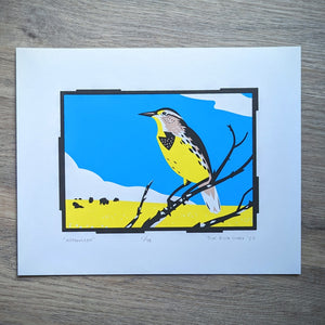 An original screen print of an illustration of a meadowlark perched on a branch in front of a big blue sky with prairie and bison in the background.