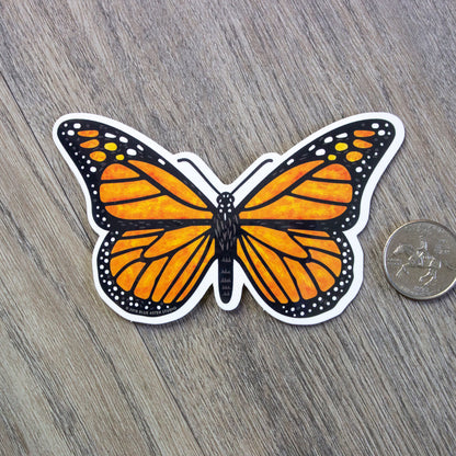 A vinyl sticker of a monarch butterfly sitting next to a US quarter for scale.