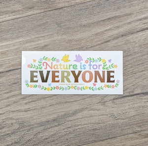 A rectangular vinyl sticker with the words "Nature Is For" in rainbow colors and "Everyone" with each leter in shades of skin tones surrounded by flowers and birds
