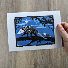 Load image into Gallery viewer, A hand holding a 5x7 inch art print of an opossum with babies on her back in a nighttime scene.