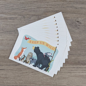 A stack of ten "Keep Us Wild" postcards with an illustration of a fox, rabbit, turtle, owl, raccoon, bear, opossum, snake, and songbird all holding a banner with the words "Keep Us Wild" on it.
