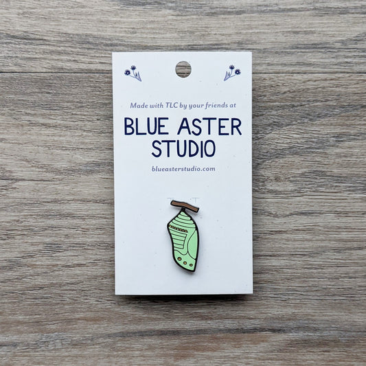 A monarch chrysalis enamel pin.
