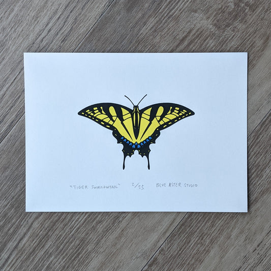 An original screen print of a tiger swallowtail butterfly. Printed in three inks of yellow, sparkly blue, and black.