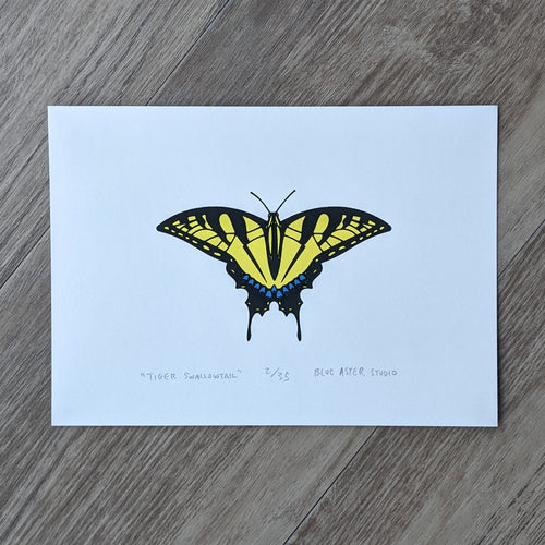 An original screen print of a tiger swallowtail butterfly. Printed in three inks of yellow, sparkly blue, and black.