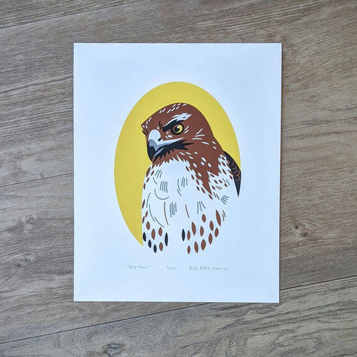 A screen printed portrait of a red-tailed hawk looking down with a yellow oval framing its body.