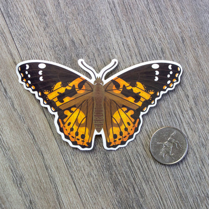 A vinyl sticker of a painted lady butterfly sitting next to a USD quarter for scale.